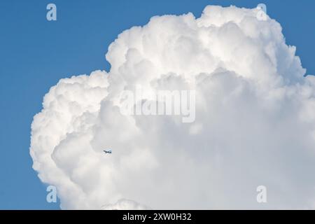 Looking up at a large fluffy cloud with a blue sky behind, and an airplane passing in front Stock Photo