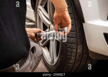 A mechanic performs tire maintenance using a wrench to tighten lug nuts on a vehicle's wheel, showcasing hands-on skills critical for automotive safet Stock Photo