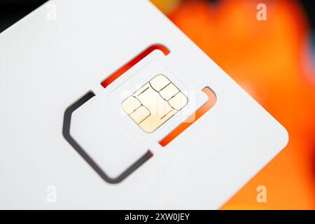 A high-resolution close-up of a SIM card with a golden chip design, set against a blurred vibrant orange background. Perfect for telecommunications, m Stock Photo