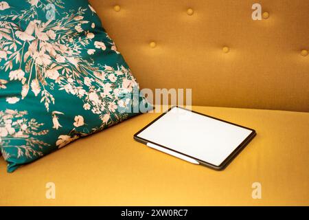 Graphic tablet on yellow sofa. Home office equipment. Real estate interior. Green pillow. Stock Photo