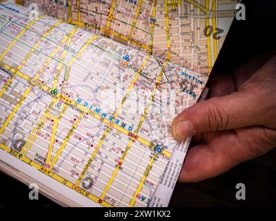Analog traveling: a New York tourist is holding in his hand a tradional tourist guide book, opened on a page with the map of Manhattan, New York. Stock Photo