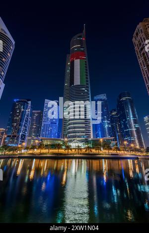 Dubai, UAE, Jan 8, 2016. Almas Tower, a 68-story skyscraper in Jumeirah Lakes Towers, with the Emirati flag, was once the tallest building of the city Stock Photo