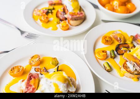 Egg Benedict with tuna, bacon, asparagus and tomatoes with hollandaise sauce on three white plates. The concept is a delicious family breakfast. Selected focus. High quality photo Stock Photo