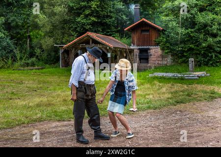 Raftsman Martin Spreng walks with journalist Angela Berg across the forecourt of the Monhardter Wasserstube near Altensteig, Baden-Württemberg, Germany. Both look down at a device in her hand. Spreng, chairman of the German Rafting Association, demonstrates historical Black Forest rafting at the site. Rafting has been recognised as UNESCO intangible cultural heritage since 2022. Stock Photo