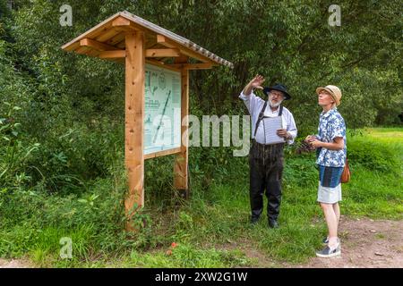 Raftsman Martin Spreng explains the construction of a typical Nagold raft to journalist Angela Berg at an information board. Spreng, chairman of the German Rafting Association, demonstrates historical Black Forest rafting at the Monhardter Wasserstube near Altensteig, Baden-Württemberg, Germany. Rafting has been recognised as UNESCO intangible cultural heritage since 2022. Stock Photo