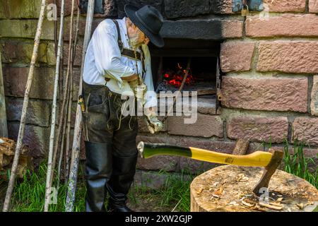 Raftsman Martin Spreng carries a long, thin wooden rod away from a pond at the edge of the Monhardter Wasserstube. Rods soaked like this were then heated, tested and twisted into "Wieden", the flexible wood strands used to bind rafts. Altensteig, Baden-Württemberg, Germany. Rafting has been recognised as UNESCO intangible cultural heritage since 2022. Stock Photo
