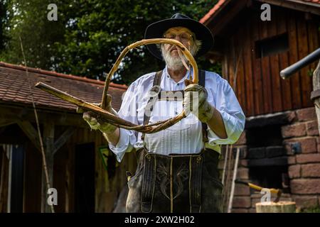 Raftsman Martin Spreng tests the flexibility of a freshly twisted "Wiede" by bending the wood strand into a ring. At the Monhardter Wasserstube near Altensteig, Baden-Württemberg, Germany, he demonstrates traditional Black Forest rafting. It has been recognised as UNESCO intangible cultural heritage since 2022. Stock Photo