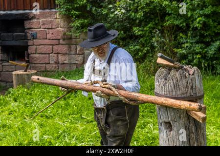 Raftsman Martin Spreng bends a heated wooden rod over the Wiedstock at the Monhardter Wasserstube near Altensteig, Baden-Württemberg, Germany. This turns the rod into a "Wiede" – a twisted wooden rope used to bind rafts. Rafting has been recognised as UNESCO intangible cultural heritage since 2022. Stock Photo