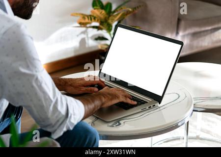 Young business man using computer laptop in front of an blank white computer screen in his home living room. Photo ready for mockup. Stock Photo