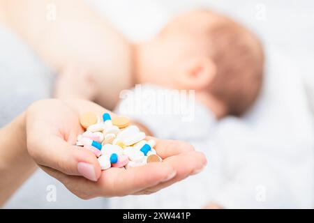 Mother holding handful of pills and tablets while breastfeeding newborn baby. Breastfeeding and medication concept Stock Photo