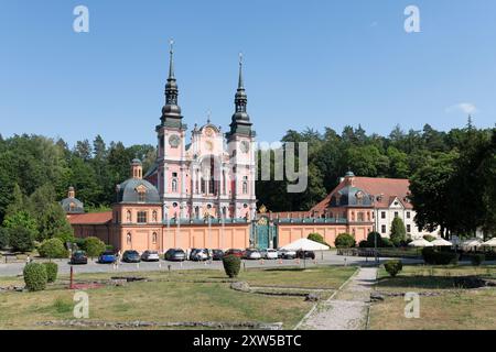 Sunlit colorful Baroque style church set against thick green foliage Stock Photo