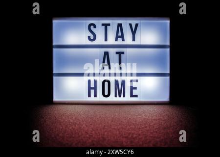 A lightbox displaying the message stay at home in bold, black letters, illuminated against a dark background. Stock Photo