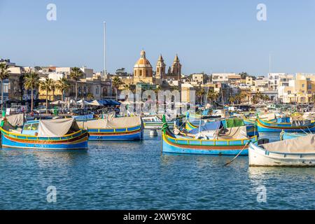 Malta, Marsaxlokk Harbor. Our Lady of Pompei church in background.Luzzijiet, plural of luzzu, colorful traditional Maltese fishing boats. Stock Photo