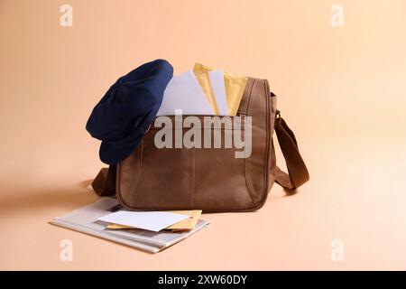 Brown postman's bag, envelopes, newspapers and hat on beige background Stock Photo