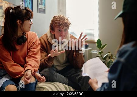 Group of young adults engaged in animated discussion about a film project in a casual, creative workspace environment, with one person facing camera and others looking away Stock Photo
