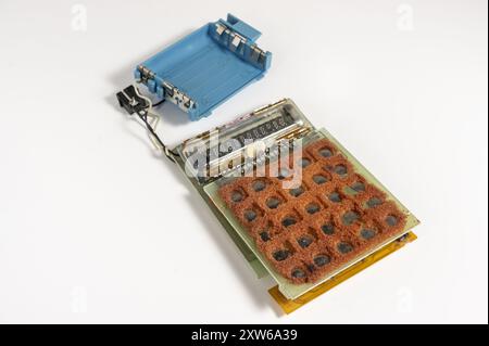 a disassembled vintage calculator with its components laid out on a white background. The calculator's internal parts are visible, including a brown, Stock Photo