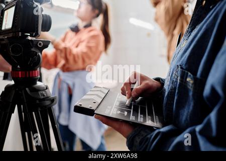 Close-up of hands holding clapperboard while filming with professional camera in indoor setting. Background showing blurred figure working with equipment Stock Photo