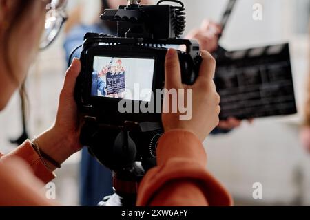 Close-up view of camera display showing clapperboard during film shoot. Person holding camera with crew member clapping in background Stock Photo