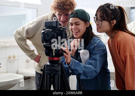 Group of three young people enthusiastically analyzing camera setup in a well-lit room while discussing project details and sharing ideas together Stock Photo
