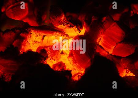 Hot coals glow orange in the dark of the stove. They show the layered structure of the wood. Close-up. Stock Photo