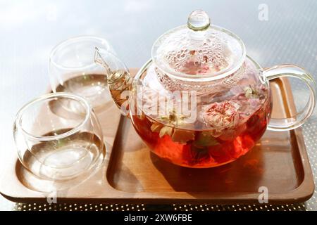 Glass pot of rose infusion tea with a pair of tea cups Stock Photo