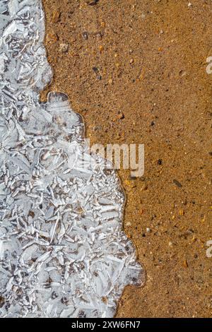 The shoreline of the reservoir on a frosty day. Openwork patterned ice and red sand in the water. Close-up. Stock Photo