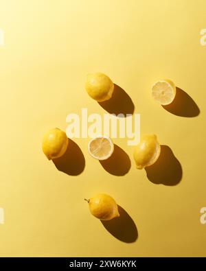 Whole and cut in half lemons on yellow background with dramatic shadows Stock Photo