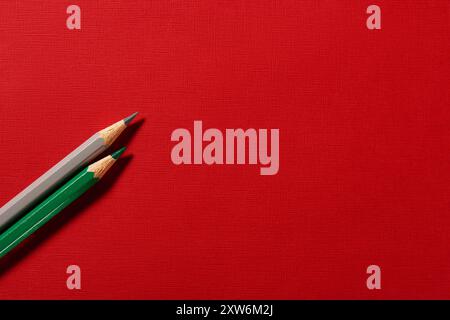 Green and gray colored pencils on red paper background with empty space Stock Photo
