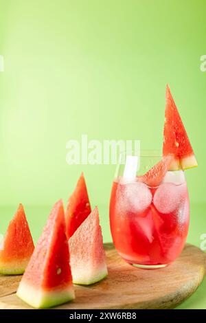 Watermelon triangles and a soft drink with ice and chunks of watermelon on top of a wooden board, neutral green background Stock Photo