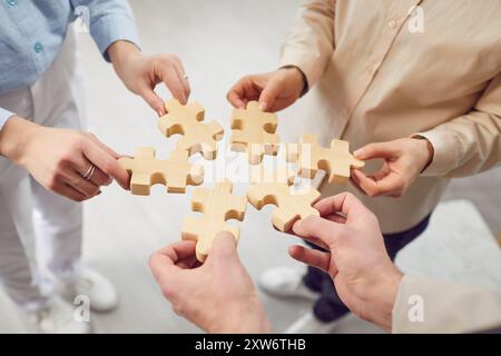 Close up photo hands of people holding diverse pieces of wooden puzzle, team assembling jigsaw  Stock Photo