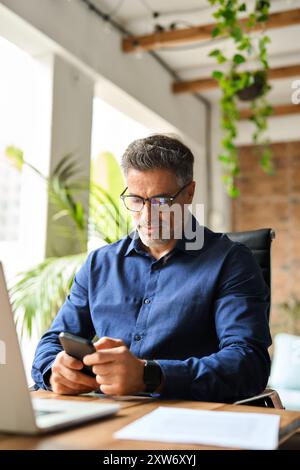 Busy middle aged professional businessman executive using smartphone at work. Stock Photo