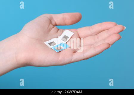 Woman holding SIM cards on light blue background, closeup Stock Photo