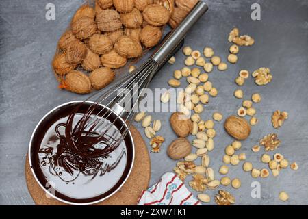 Homemade chocolate in making. Chocolate ganache with hazelnuts and walnuts on a gray background with space for text. Stock Photo