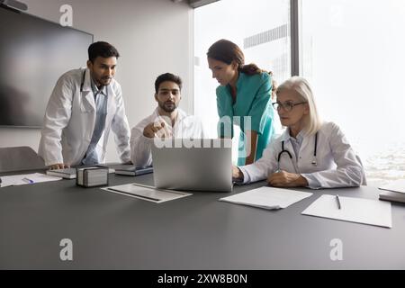 Young and mature internists gathered around laptop in meeting room Stock Photo