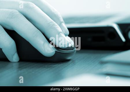 Detailed view of a person's hand using a mouse next to a laptop on a desk Stock Photo