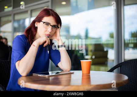 pensive woman thinking in a coffee shop terrace in the street while using a tablet Stock Photo