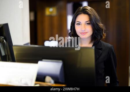 Happy female receptionist standing at hotel counter Stock Photo