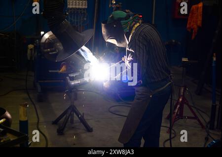 Skilled welder in protective gear performing welding in a workshop with sparks flying Stock Photo