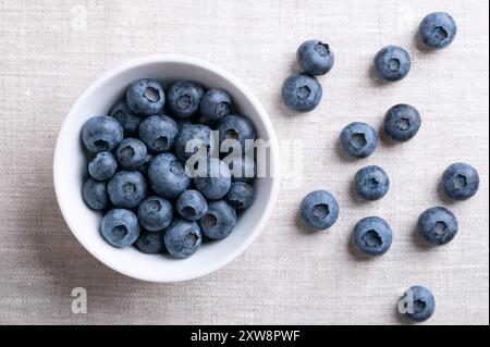 Blueberries in a white bowl on linen fabric. Dark blue colored, ripe, raw berries, fruits of Vaccinium corymbosum, cultivated blueberries. Stock Photo