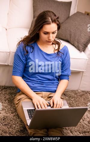 Young woman works from home on her laptop in a cozy living room, typing with focus Stock Photo