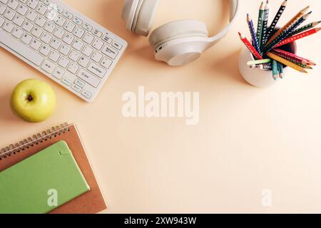 Headphones, keyboard, notepad, pens and apple on neutral beige background. Back to school concept. Top view, flat lay, copy space. Stock Photo