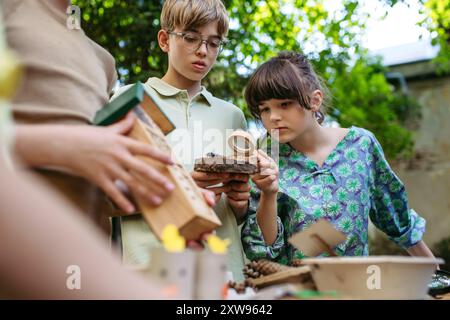 Children looking at models of insect with magnifying glass, learning about wildlife during outdoor sustainable educational class. Stock Photo