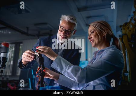 Two robotics engineers working on new project, calibring robotic prosthetic hand. Concept of modern technology in industries, automated processes Stock Photo