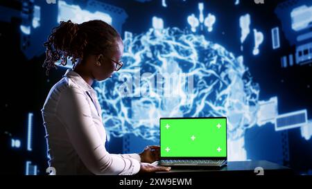 Admin updating AI systems using chroma key laptop, writing intricate binary code scripts. Technical support consultant using programming to upgrade simulation model, using AR to visualize result Stock Photo