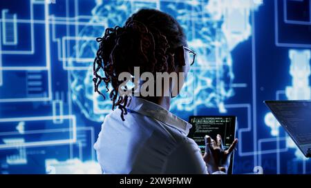 Engineering coworkers updating AI systems, writing intricate binary code scripts on tablet and laptop. Trained technicians using programming to upgrade artificial intelligence simulation model Stock Photo
