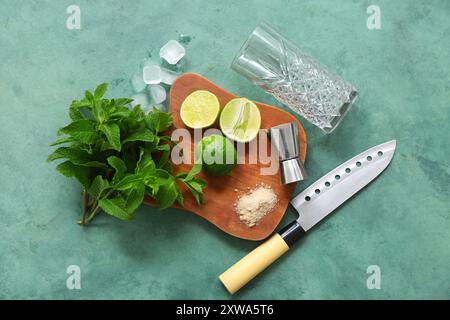 Wooden cutting board, measure cup, knife and ingredients for mojito on green background Stock Photo