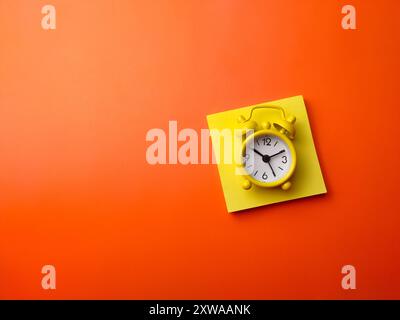 Top view sticky note and alarm clock on a orange background with copy and text space. Stock Photo
