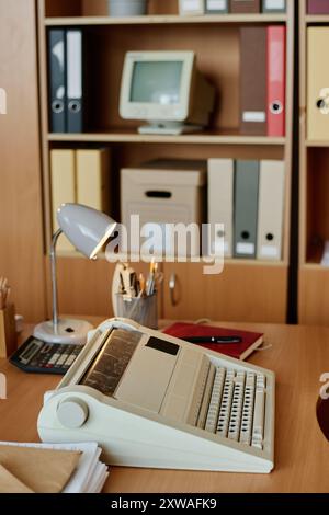 Office workspace featuring neatly arranged documents, office supplies, and vintage typewriter against background of wooden shelves holding files and storage boxes Stock Photo