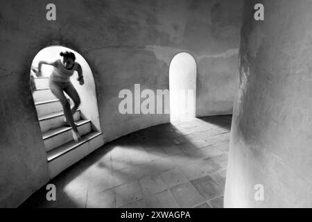 An unknown female holding hands with children walks down the stairs in the dark ancient basement, sunbeam shines through the tunnel onto the staircase Stock Photo