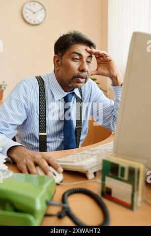 Man sitting at desk in office, wearing shirt and tie, using desktop computer, looking tired and stressed, resting head on hand Stock Photo
